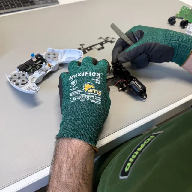 Tehnician demontează un controller alb, cu carcasa deschisă și placa scoasă alături